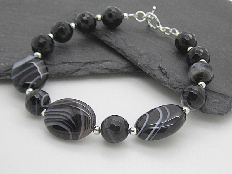Puede incluir: Pulsera de &aacute;gata negra y blanca con cierre de plata. La pulsera presenta cuentas ovaladas y redondas con un patr&oacute;n de rayas blancas y negras.