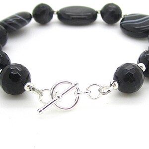 Puede incluir: Pulsera de piedras preciosas de &oacute;nix negro con cierre de palanca plateado. La pulsera presenta cuentas redondas y ovaladas.