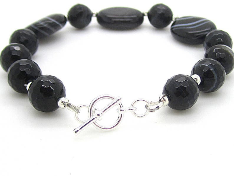 Puede incluir: Pulsera de piedras preciosas de &oacute;nix negro con cierre de palanca plateado. La pulsera presenta cuentas redondas y ovaladas.