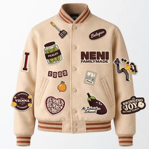 Puede incluir: Una chaqueta estilo universitario de color beige con ribetes de canalé a rayas marrones, con varios parches bordados que incluyen un tarro de pepinillos, una espátula, una berenjena, una naranja y textos como NENI FAMILYMADE, 2009, Balagan y BRINGING JOY TO THE TABLE.