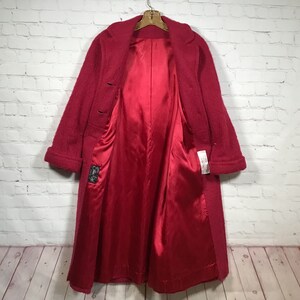 Puede incluir: Un abrigo largo de lana roja con forro de sat&eacute;n. El abrigo tiene cuello y dos botones. El abrigo est&aacute; colgado en una percha.