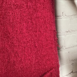 Puede incluir: Primer plano de un su&eacute;ter rojo oscuro y peludo con un bolsillo en la parte inferior. El su&eacute;ter tiene un borde deshilachado en el lado derecho.