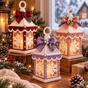 May include: Three decorative lanterns featuring crocheted covers in red, lavender, and pink. Each lantern has a scalloped roof, a top bow, white snowflake motifs on the sides, and a small hanging loop at the peak with a candle inside.