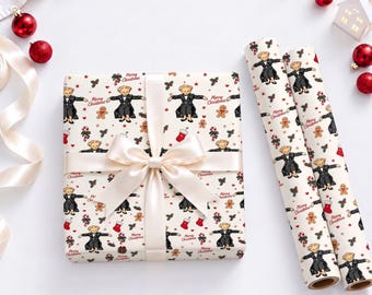 Op de afbeelding: Een vierkante geschenkdoos verpakt in crèmekleurig papier met een herhalend patroon van teddyberen in zwarte pakken, peperkoekmannetjes, zuurstokken en rode sokken, gestrikt met een crèmekleurig satijnen lint, naast twee bijpassende rollen inpakpapier.