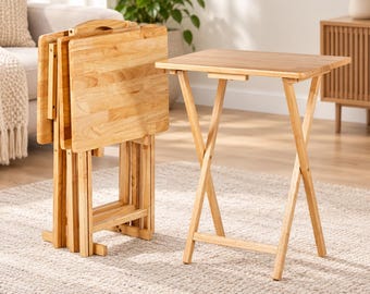 May include: A set of four light-colored wooden folding snack tables. One table is fully unfolded and standing upright, while the other three are folded flat and stacked together in a vertical storage rack made of matching wood.