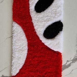 May include: A rectangular tufted rug featuring a high-pile texture with a bold graphic design. The pattern consists of vibrant red, crisp white, and deep black yarn sections arranged in curved, abstract shapes across the entire surface area.