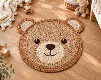 Puede incluir: Una alfombra redonda de ganchillo con forma de cara de oso. La alfombra presenta una sección principal de color marrón claro, un hocico y orejas internas de color crema, y ojos, nariz y boca bordados en marrón oscuro sobre una superficie de hilo.
