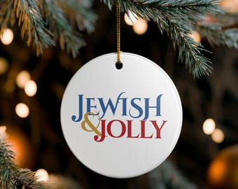 May include: A round white ceramic ornament hanging from a gold string. The ornament features the text JEWISH in blue, an ampersand in gold, and JOLLY in red. The design is centered on the smooth surface of the circular hanging decoration.
