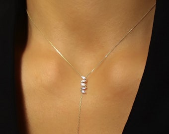 May include: A long gold chain necklace with a pendant featuring a vertical row of five small, clear, marquise-shaped stones.