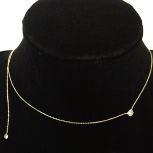 May include: A delicate gold chain necklace with two small, clear gemstones. The necklace is on a black velvet display stand.
