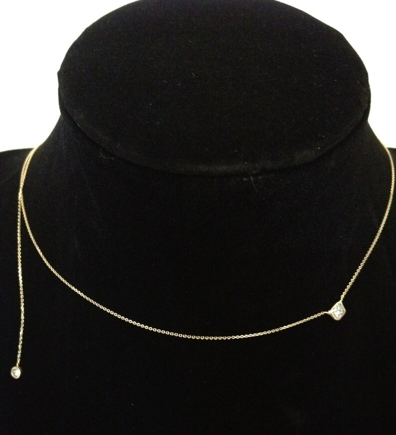 May include: A delicate gold chain necklace with two small, clear gemstones. The necklace is on a black velvet display stand.