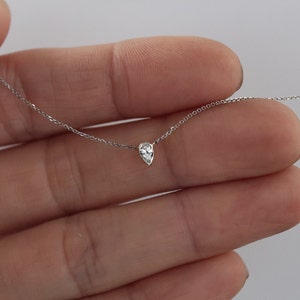 May include: A delicate silver chain necklace with a single pear-shaped clear gemstone pendant.