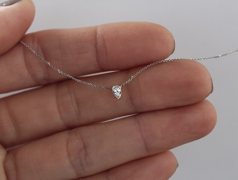 May include: A delicate silver chain necklace with a single pear-shaped clear gemstone pendant.
