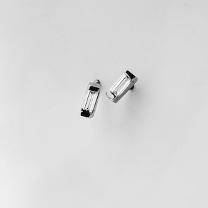 May include: A pair of silver earrings with a baguette-shaped diamond in each earring.