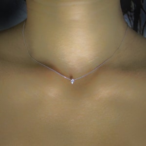 May include: A delicate silver chain necklace with a small, teardrop-shaped pendant.