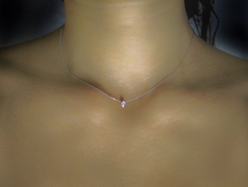 May include: A delicate silver chain necklace with a small, teardrop-shaped pendant.