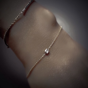 K&ouml;nnte beinhalten: Ein zartes Armband aus Goldkette mit einem einzigen, quadratischen Diamanten als Anh&auml;nger.