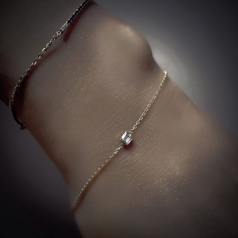 K&ouml;nnte beinhalten: Ein zartes Armband aus Goldkette mit einem einzigen, quadratischen Diamanten als Anh&auml;nger.