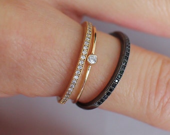 Op de afbeelding: Twee gouden ringen met een enkele diamant op een ring. De ene ring is bezet met kleine diamanten en de andere met zwarte diamanten.