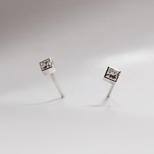 May include: A pair of silver stud earrings with a clear square-shaped gemstone in the center of each earring.