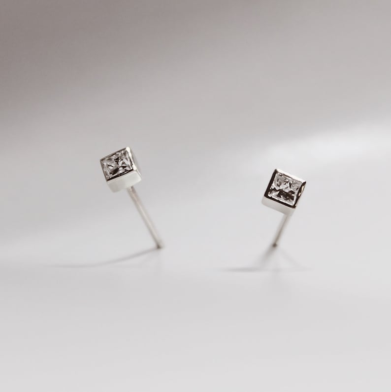 May include: A pair of silver stud earrings with a clear square-shaped gemstone in the center of each earring.