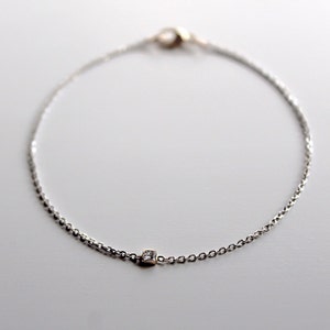 May include: A delicate silver chain bracelet with a single square-shaped diamond accent.