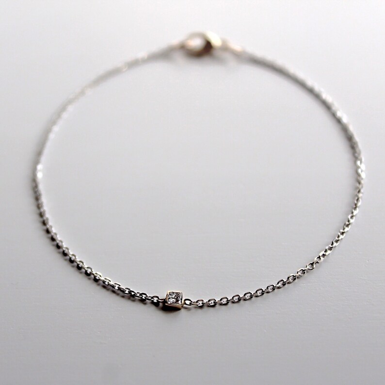 May include: A delicate silver chain bracelet with a single square-shaped diamond accent.