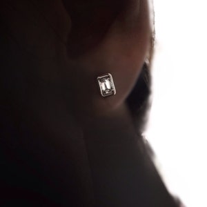 Puede incluir: Primer plano de una oreja con un peque&ntilde;o pendiente rectangular transparente.