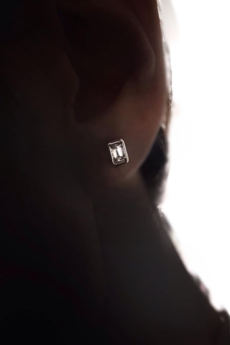 Puede incluir: Primer plano de una oreja con un peque&ntilde;o pendiente rectangular transparente.