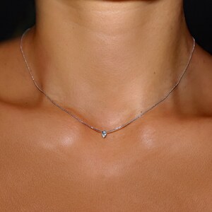 May include: A delicate silver chain necklace with a small pear-shaped pendant.