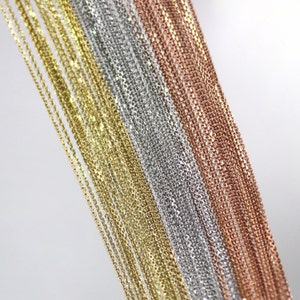 May include: A close-up of multiple gold, silver, and rose gold chains. The chains are arranged in rows, with the gold chains on the left, the silver chains in the middle, and the rose gold chains on the right.