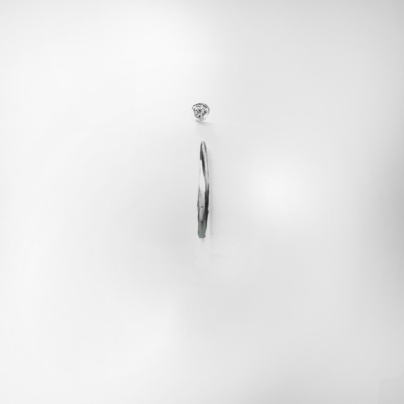 Op de afbeelding: Een zilveren oorring met een enkele heldere diamant die in de bovenkant van de oorring is gezet.