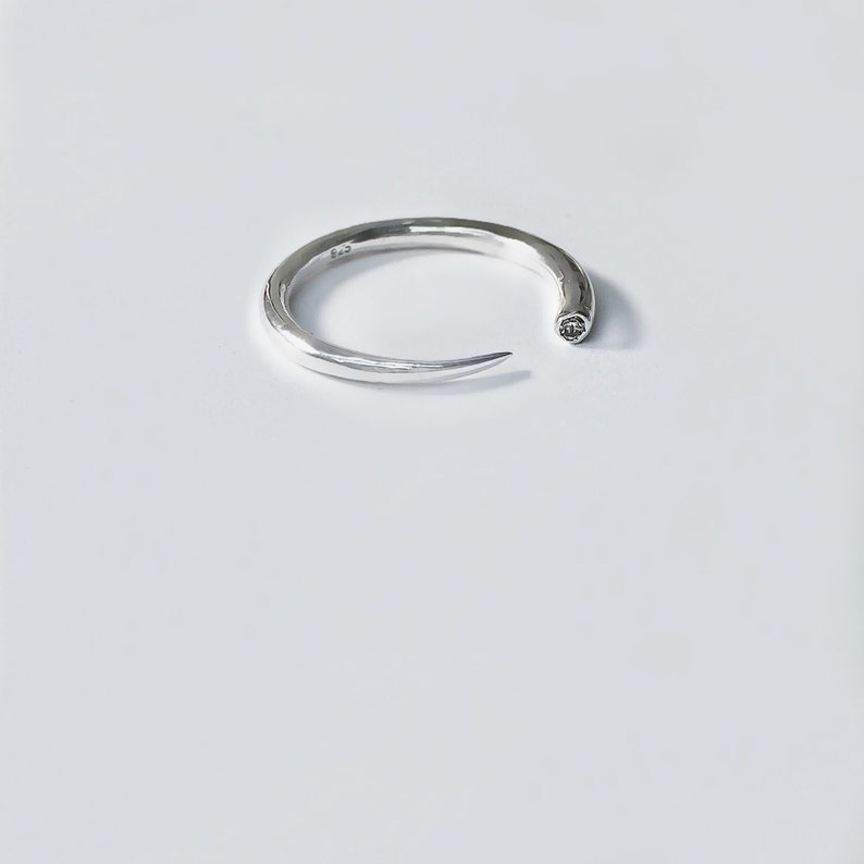 Op de afbeelding: Een zilveren ring met een puntig uiteinde en een kleine diamant die in het metaal is gezet.