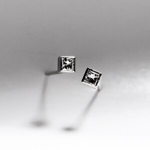 May include: A pair of silver stud earrings with square-shaped clear gemstones.