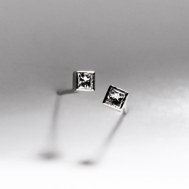 May include: A pair of silver stud earrings with square-shaped clear gemstones.
