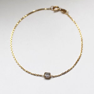 K&ouml;nnte beinhalten: Ein zartes Armband aus einer goldenen Kette mit einem einzigen, klaren, rechteckigen Edelstein.