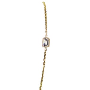 K&ouml;nnte beinhalten: Ein zartes Armband aus einer goldenen Kette mit einem einzigen, klaren Smaragdschliff-Edelstein.