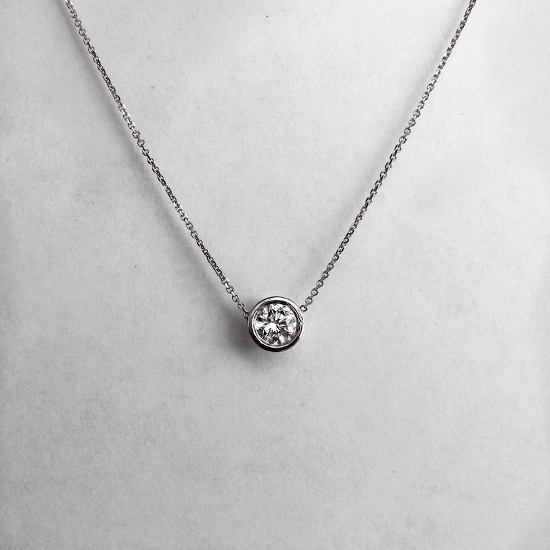 May include: A silver chain necklace with a round, bezel-set diamond pendant.