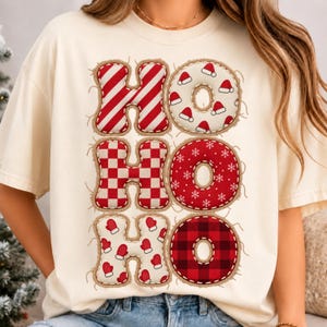 Peut inclure: Un t-shirt à manches courtes couleur crème avec le texte HOHO HOHO HOHO imprimé en trois lignes. Les lettres présentent un aspect appliqué à bords effilochés avec divers motifs rouges et blancs, incluant des rayures, carreaux et flocons.