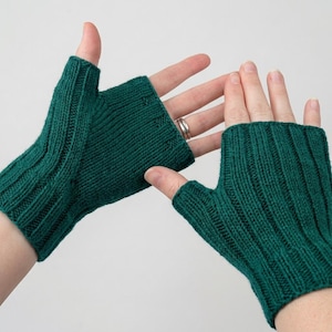 May include: A pair of dark teal fingerless gloves featuring a ribbed knit texture. The gloves cover the palm and back of the hand while leaving the fingers exposed. The knit pattern includes vertical columns of stitches that provide a textured appearance.