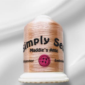 Peut inclure: Une bobine de fil à broder de couleur pêche avec le texte "Simply Sew Maddie's Attic" et un bouton rose à quatre trous.