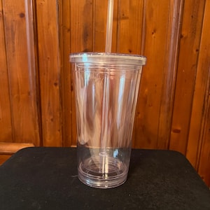 Puede incluir: Un vaso transparente de plástico con tapa y una pajita. El vaso está vacío y tiene un acabado liso y transparente.