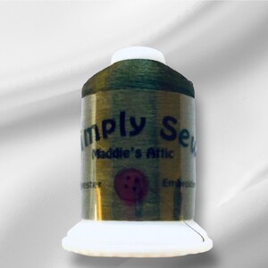 Peut inclure: Une bobine de fil à broder vert avec l'étiquette "Simply Sew Maddie's Attic" et un graphique de bouton rouge.