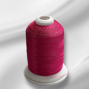 May include: A spool of bright pink thread wound on a white plastic bobbin.