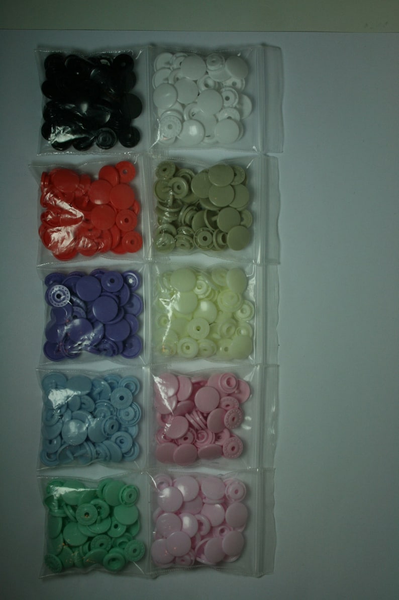 May include: Assortment of plastic snap buttons in various colors, including black, white, red, purple, light blue, green, and pink. The buttons are packaged in clear plastic bags.