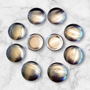 May include: Ten silver-colored round metal buttons, arranged in a circle on a white marble surface.