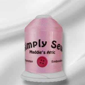Peut inclure: Une bobine de fil à broder rose avec le texte "Simply Sew Maddie's Attic" et un bouton rouge.