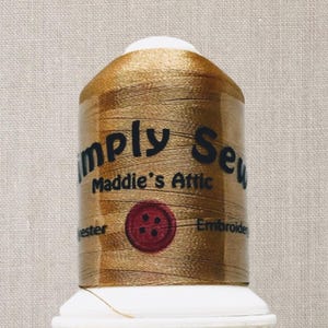 Peut inclure: Une bobine de fil à broder doré avec le texte "Simply Sew Maddie's Attic" et un bouton rouge à quatre trous.