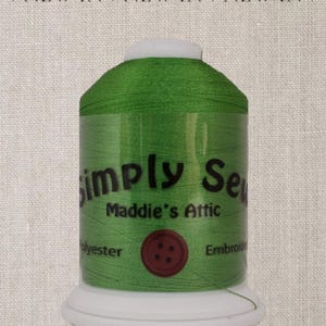 May include: A spool of green embroidery thread with the brand name "Simply Sew" and the text "Maddie's Attic" on the label. The spool has a white plastic base and a red button with four holes.