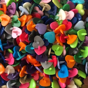 Puede incluir: Un gran surtido de botones de pl&aacute;stico en forma de coraz&oacute;n de varios colores. Los botones son de varios tonos de rojo, naranja, amarillo, verde, azul, morado, rosa y blanco.